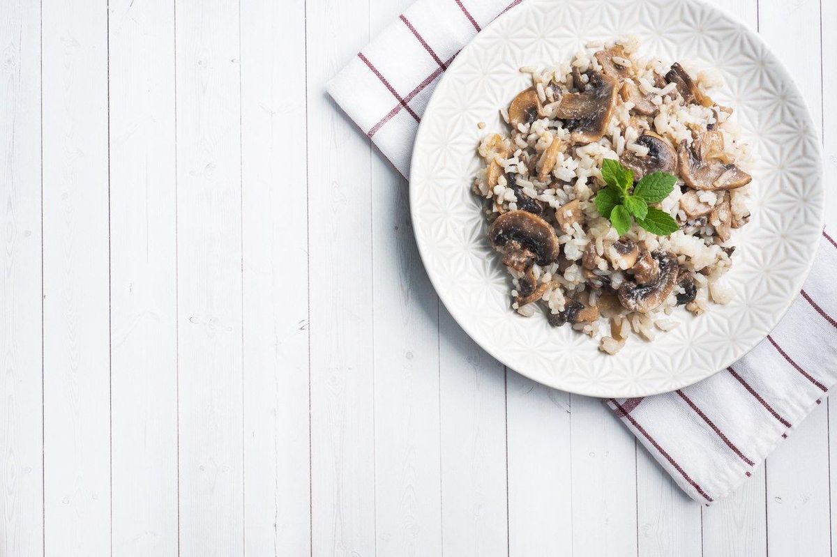 Risotto crémeux aux champignons, servi dans une assiette blanche, avec copeaux de parmesan et herbes fraîches.